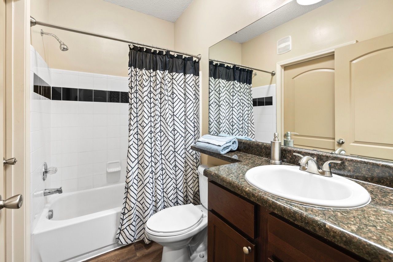 Bathroom with tub/shower, toilet, granite vanity, and large mirror.