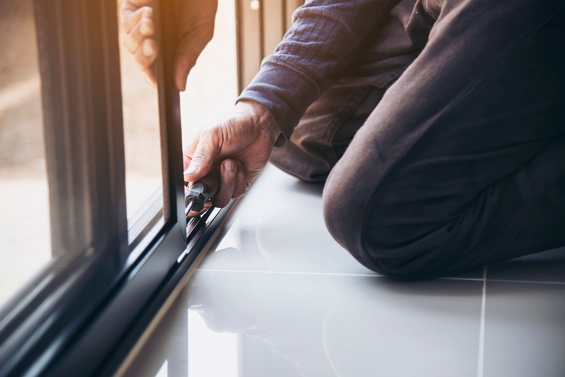 A man is working on installing an aluminum frame for a wire screen door and window at a construction site.