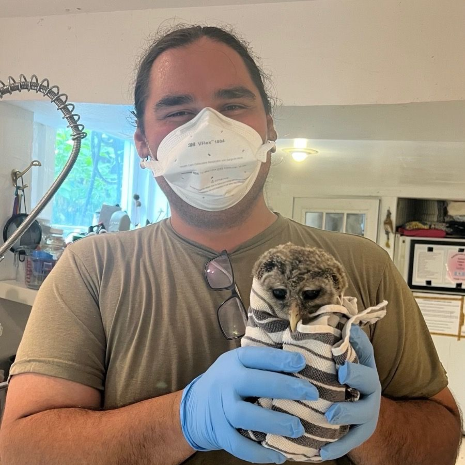 Man in mask and gloves holding a wrapped owl indoors.