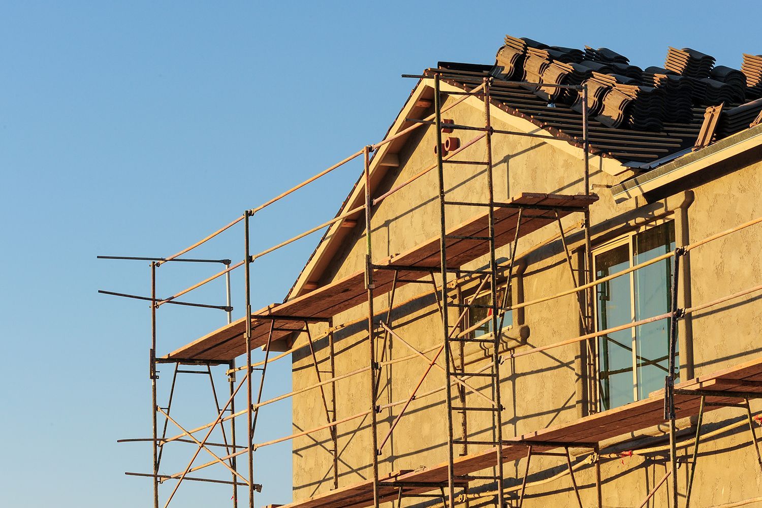 A house under construction is covered with scaffolding and roof tiles.