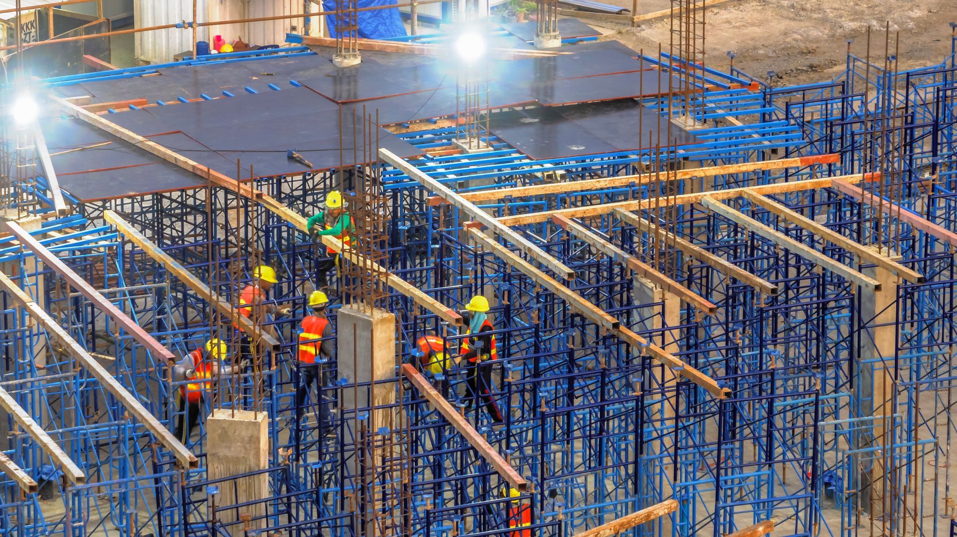Construction workers in safety gear working on a building site with scaffolding and beams.