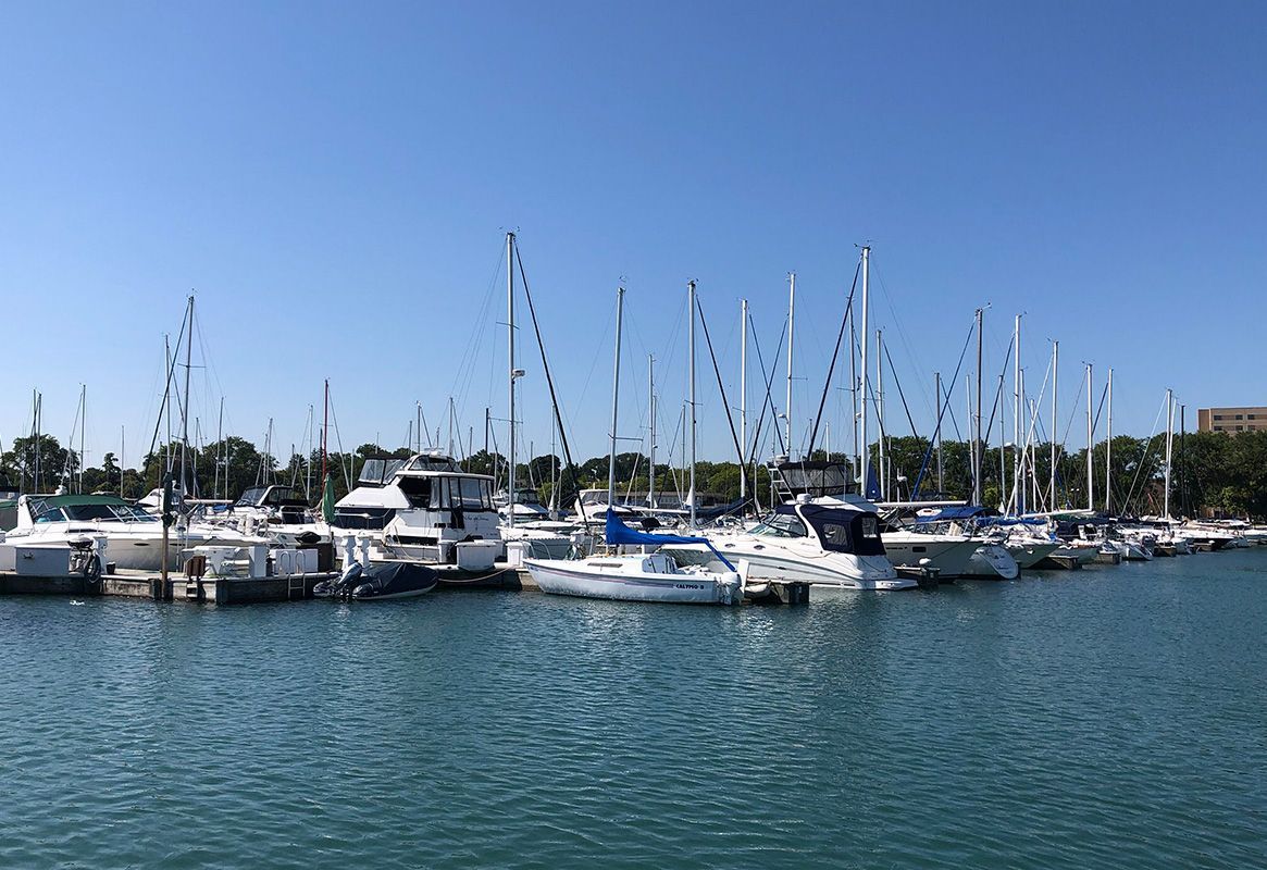 Marina with docked sailboats and yachts on calm blue water under a clear sky