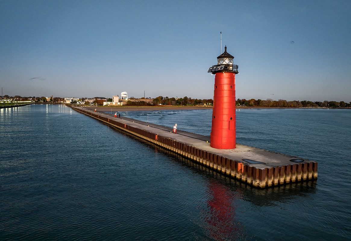 Red lighthouse on a long pier extending into calm blue water at sunset