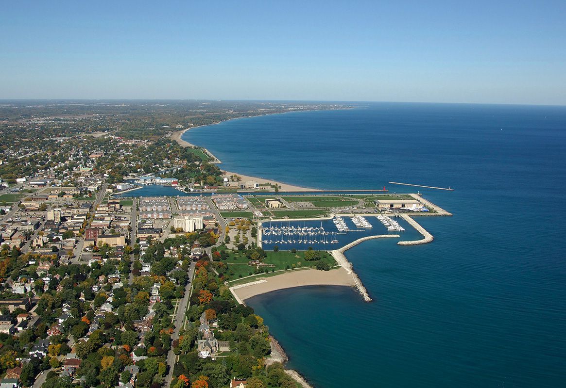 Aerial view of a coastal city with a marina and deep blue ocean under a clear sky