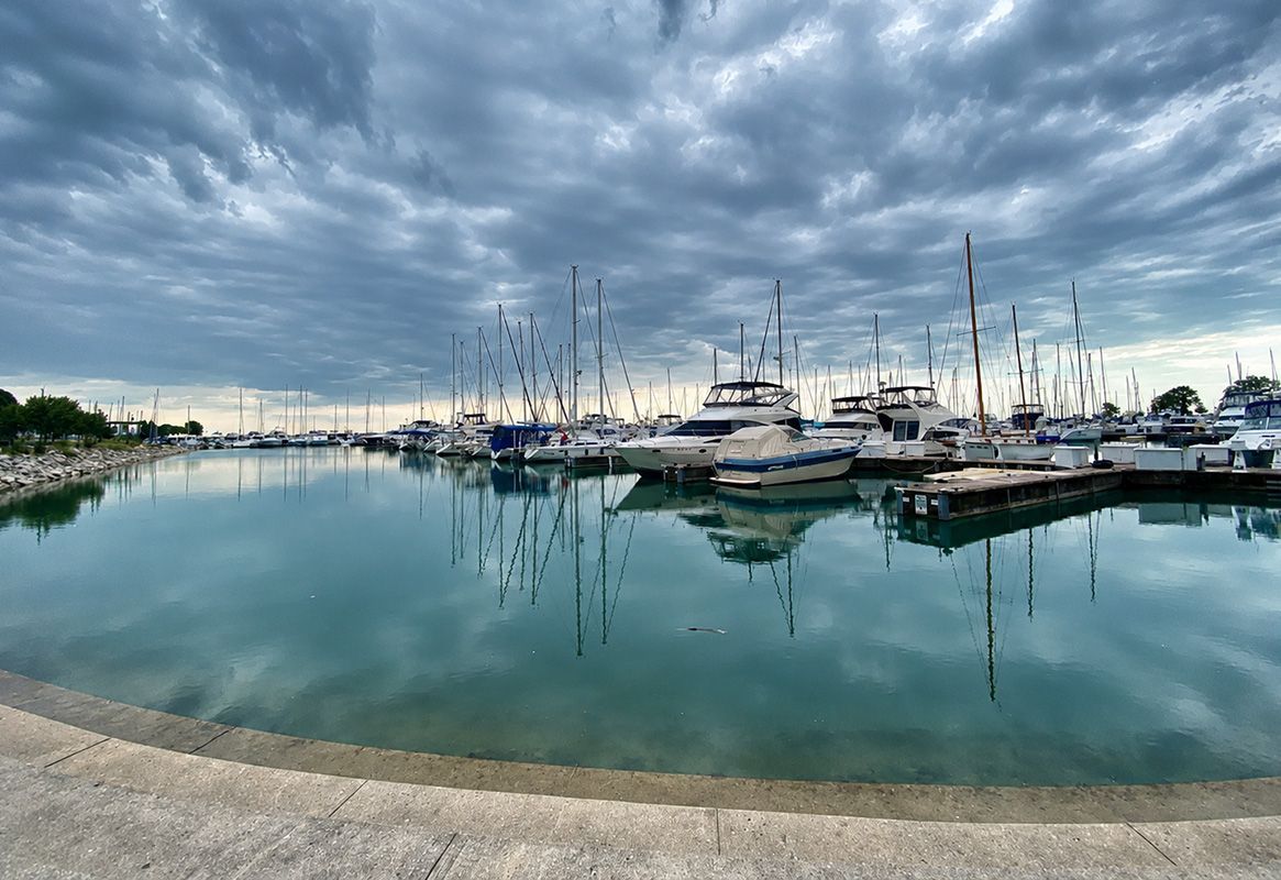 Marina with docked boats reflected in calm water under a cloudy sky