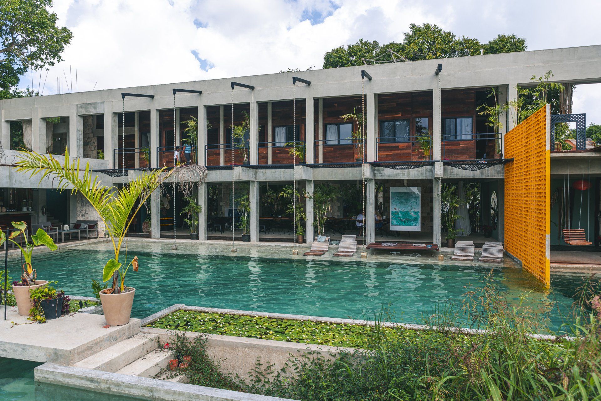 Un resort con piscina, edificio de dos pisos con columnas de hormigón, paredes de ladrillo y una pared amarilla.