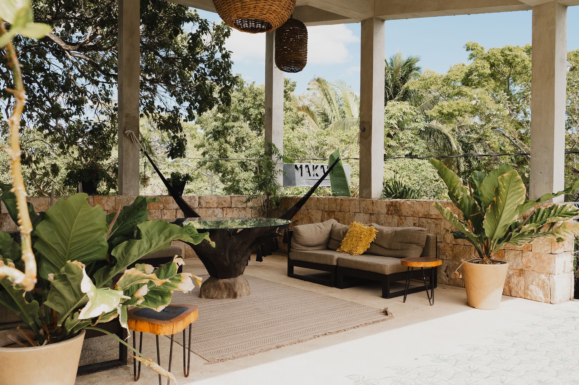 Patio con sofá, plantas y hamaca con vista a frondosos árboles.