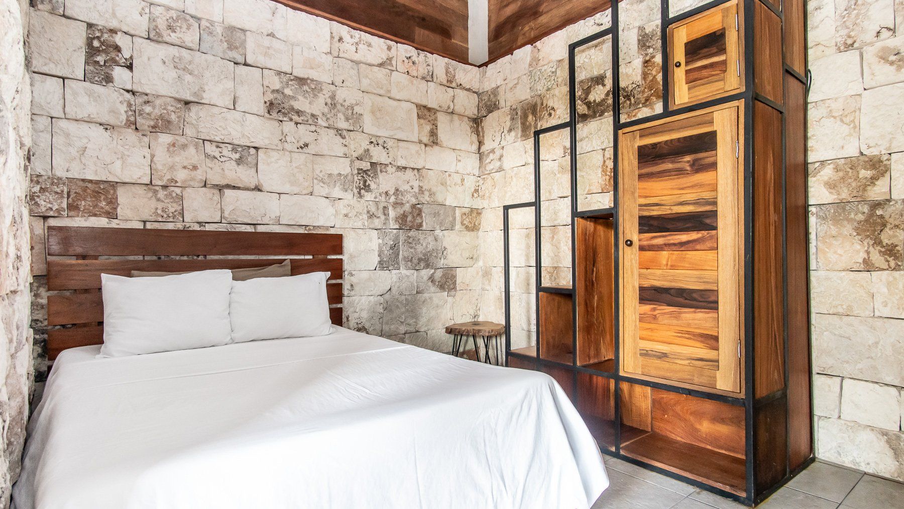 Dormitorio con paredes de piedra, cama y mueble de almacenaje de madera.