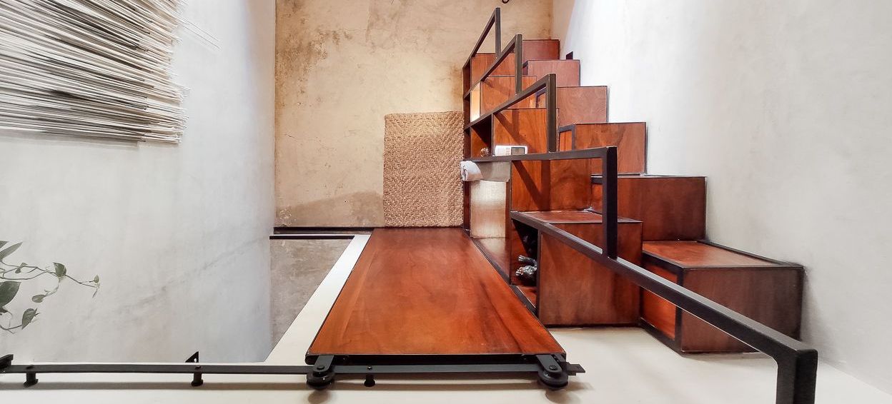 Escalera de madera con espacio de almacenamiento incorporado. Madera marrón oscuro y barandilla negra contra una pared clara.