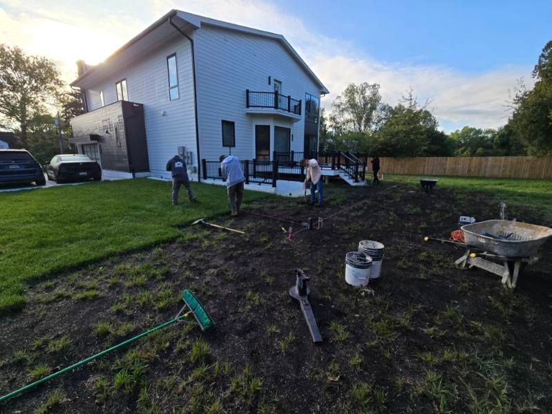 Construction workers landscaping around a modern two-story home with a deck.