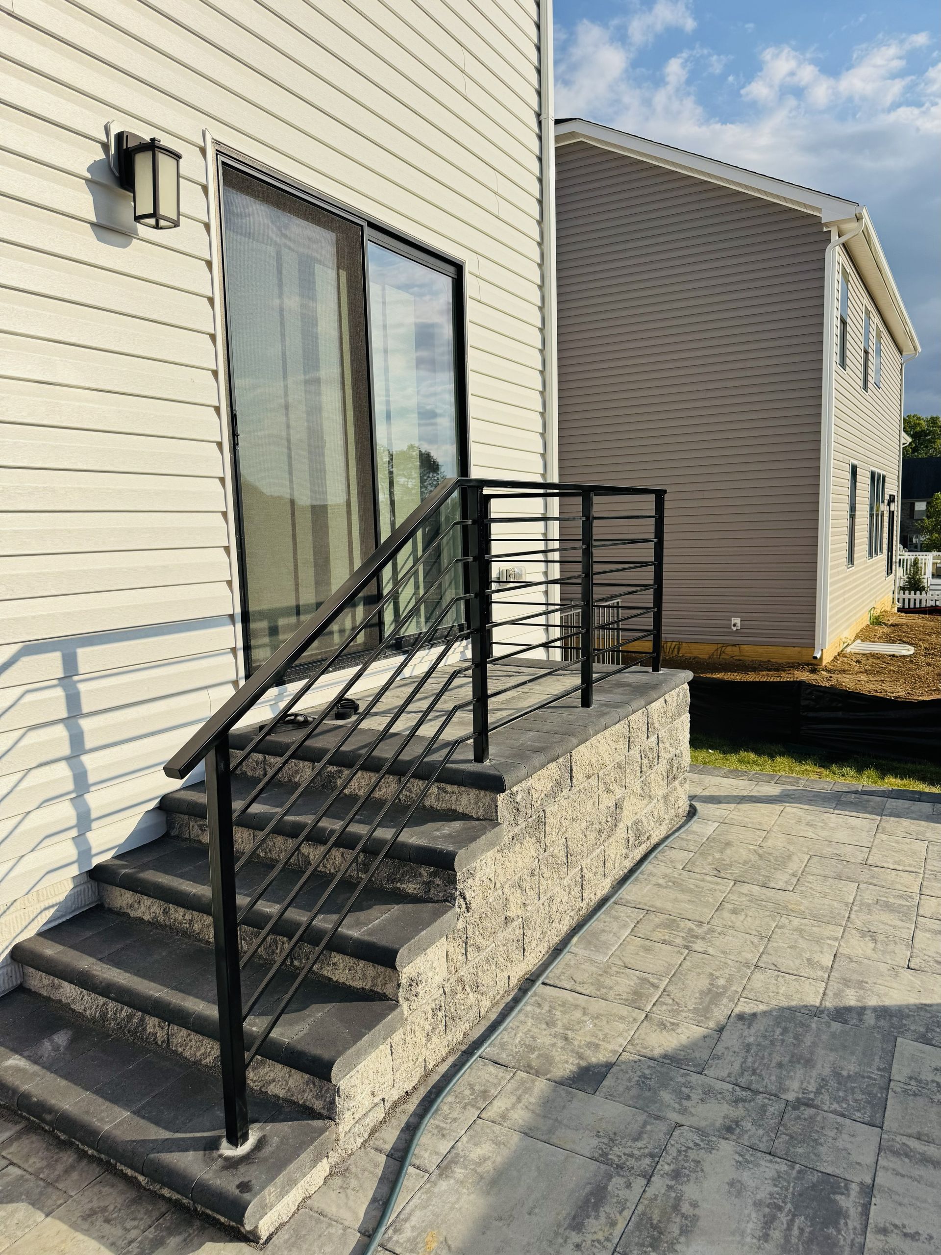 Exterior view: Steps leading to a sliding glass door, black railing, light-colored walls, gray stone steps, and patio.