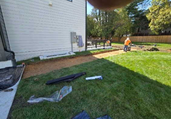 Construction workers digging a trench near a house with new grass. One worker pushes a wheelbarrow.
