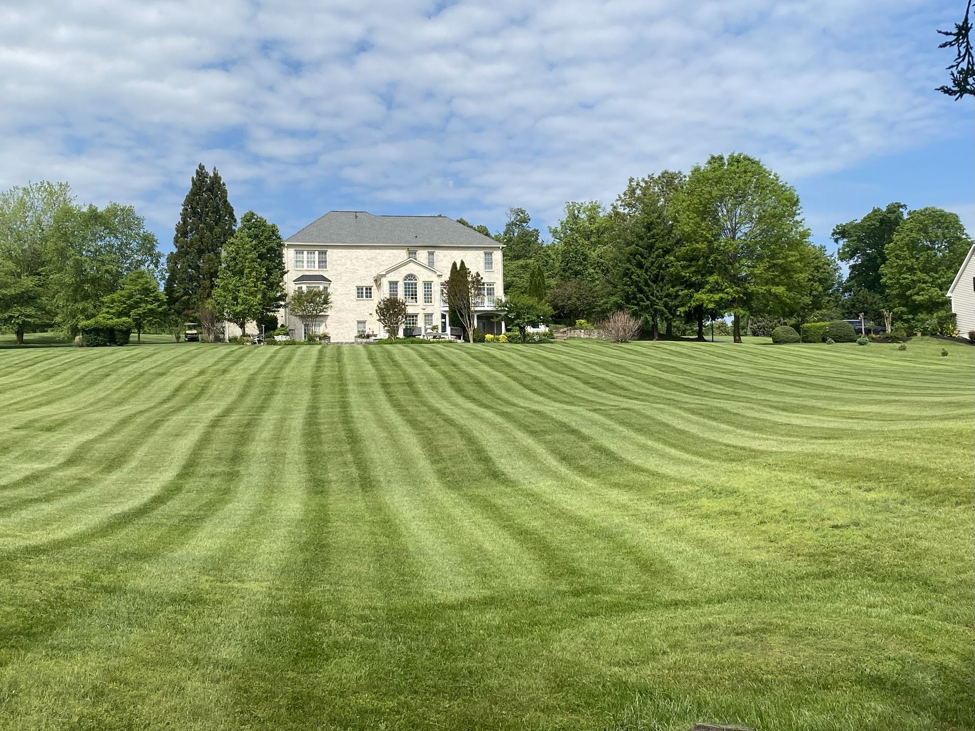 Lawn mowed with alternating light and dark stripes in front of a large house under a cloudy sky.