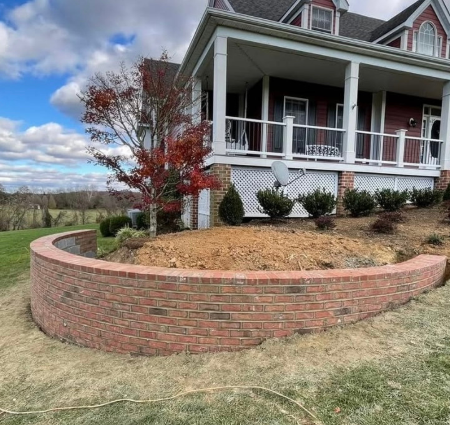 Curved brick retaining wall in front of a red house with a white porch.