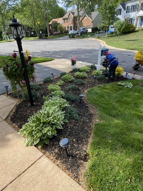 Two workers planting flowers in a front yard garden beside a driveway and lawn