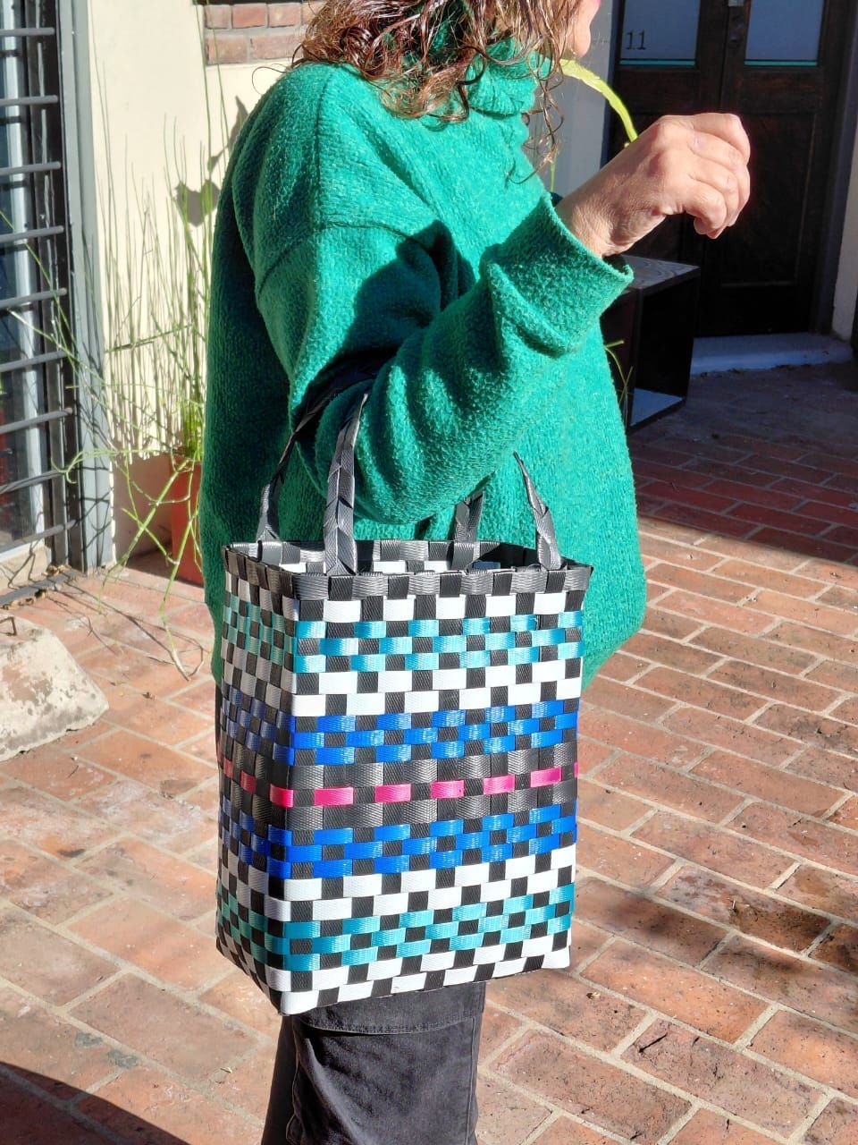 Una mujer con un suéter verde sostiene una bolsa tejida.