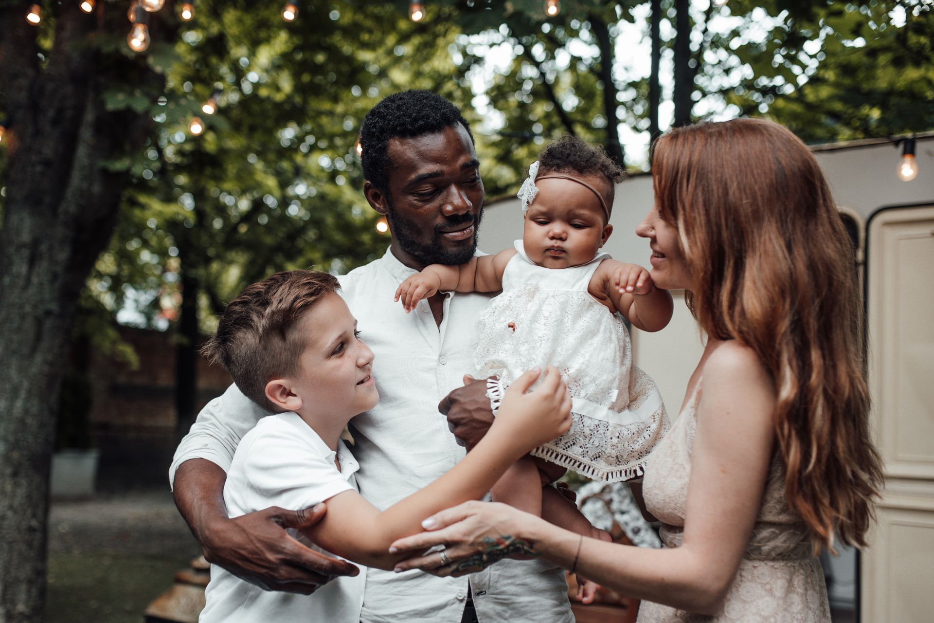 Family of four outdoors, Black father holding baby, mother and son looking on.