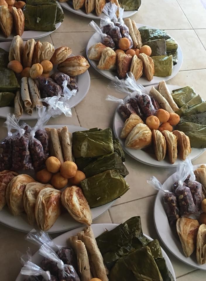 Platos de postres variados del sudeste asiático: pasteles, tortas de arroz, dulces envueltos y frutas de color naranja.