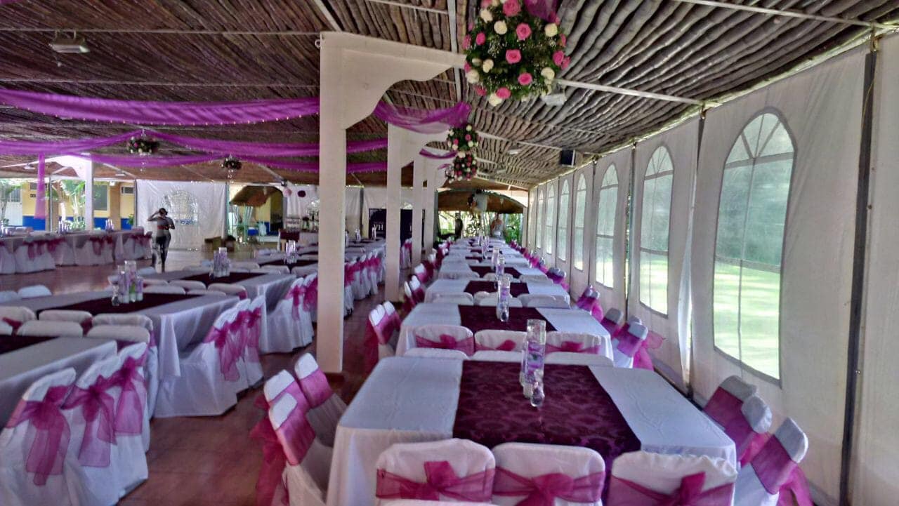 Espacio para eventos largo y decorado con mesas blancas, detalles en morado y techo de madera.