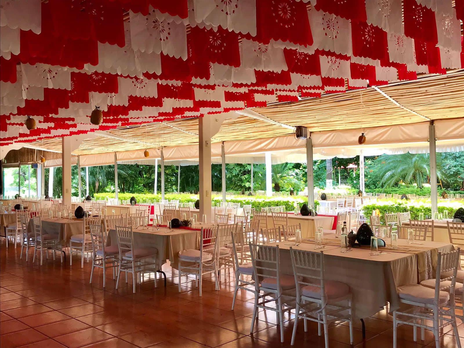 Salón de banquetes con mesas preparadas para celebración, decorado con banderas de papel rojo y blanco.