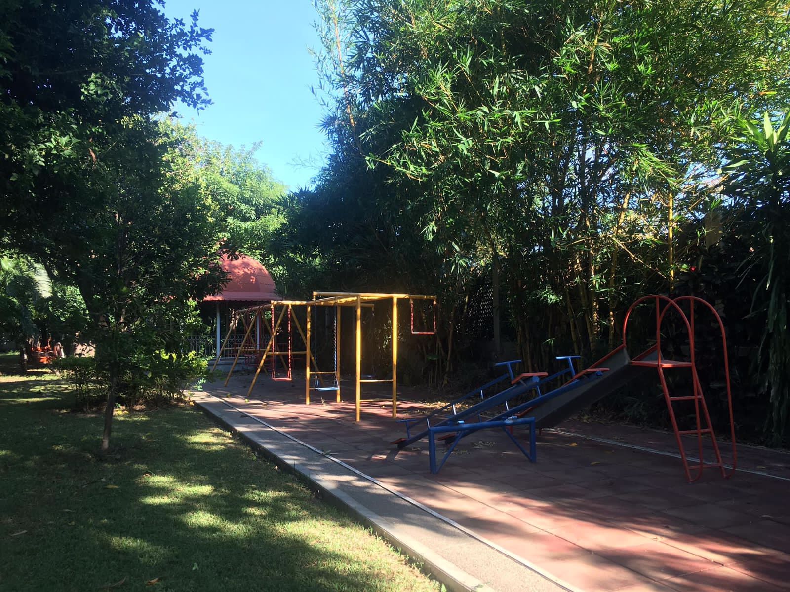 Parque infantil con columpios, balancín y tobogán en un día soleado.