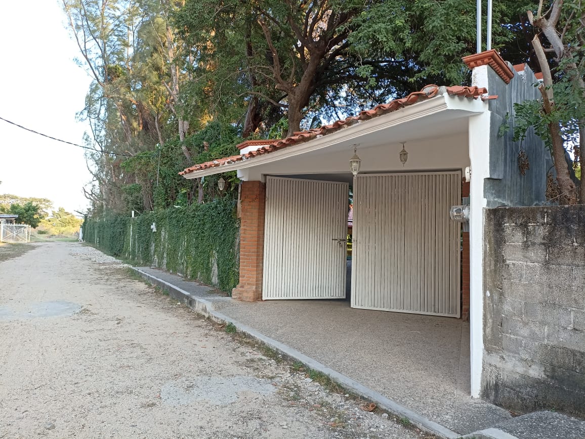 Entrada con puertas blancas, techo de tejas rojas y camino de grava. Enredaderas verdes cubren una pared.