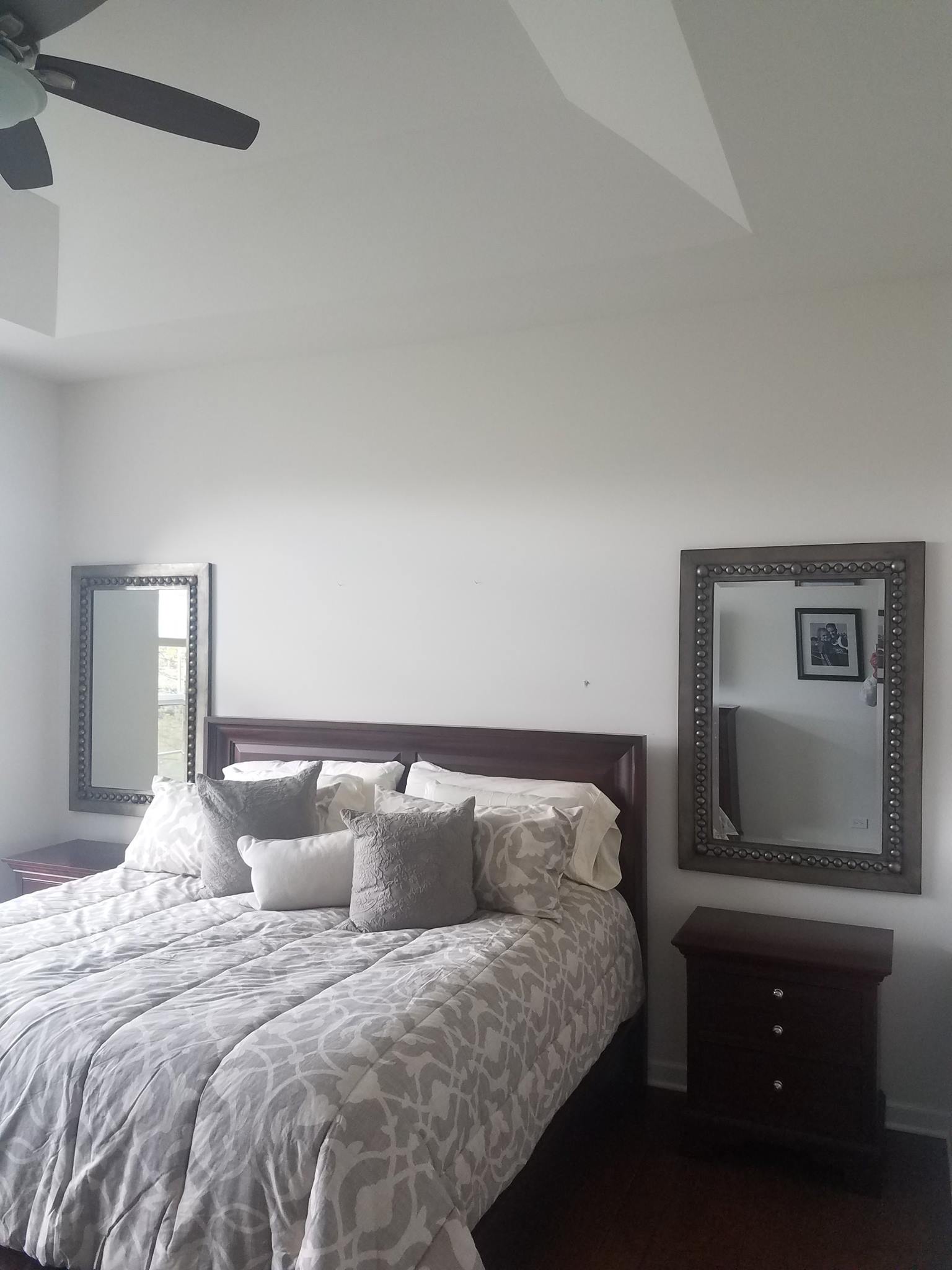 A bedroom with a bed , two mirrors and a ceiling fan.