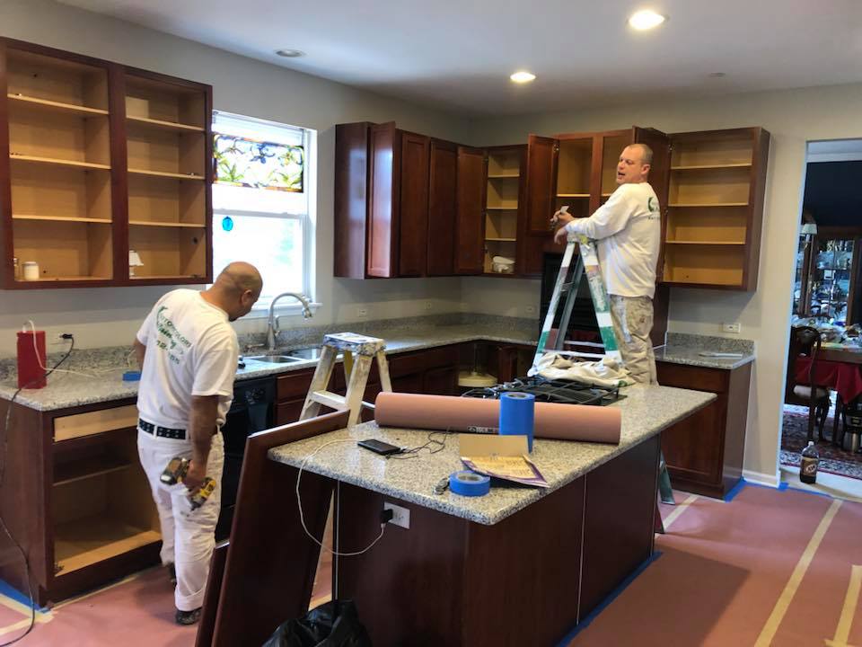 Two men are painting cabinets in a kitchen.