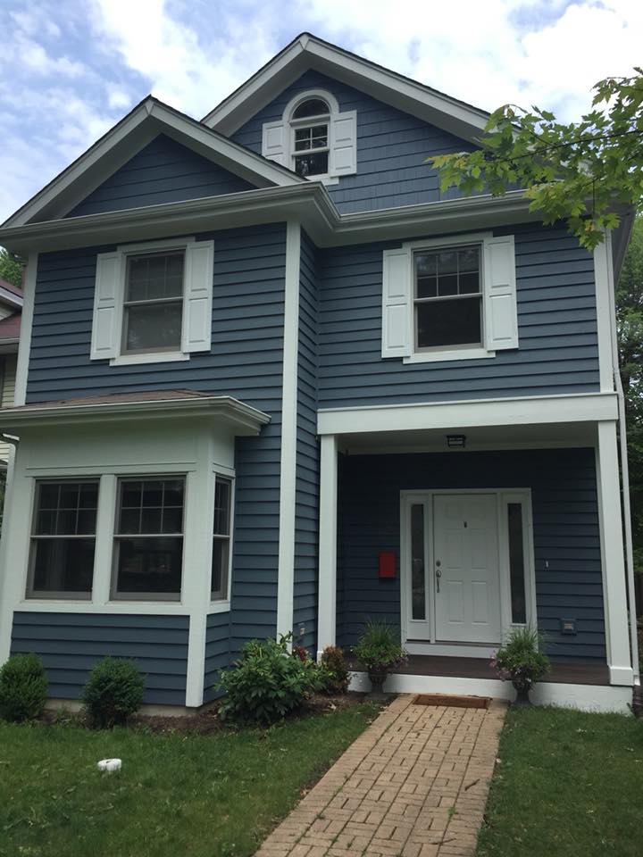 A blue house with white shutters and a brick walkway leading to the front door.