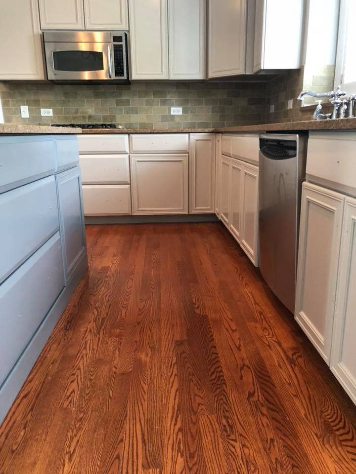 A kitchen with hardwood floors , white cabinets and stainless steel appliances.