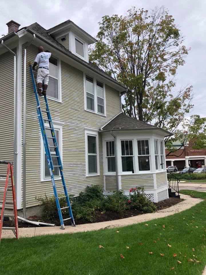 A man is standing on a ladder painting the side of a house.