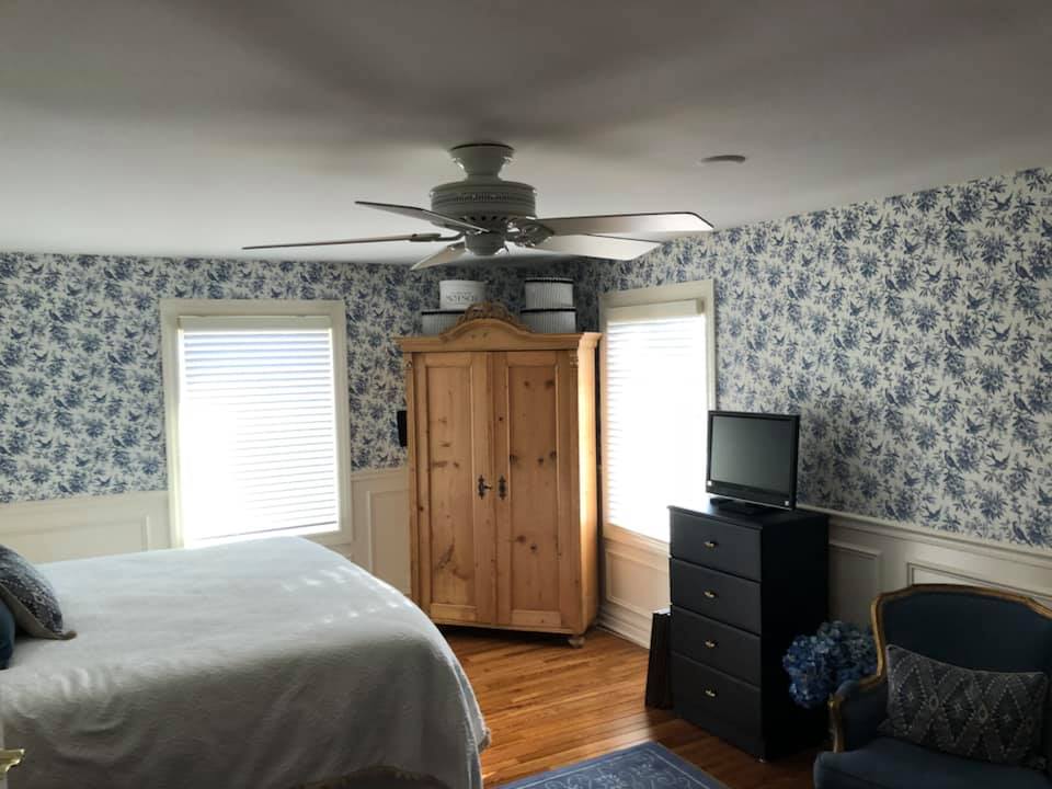 A bedroom with a bed , dresser , chair , television and ceiling fan.