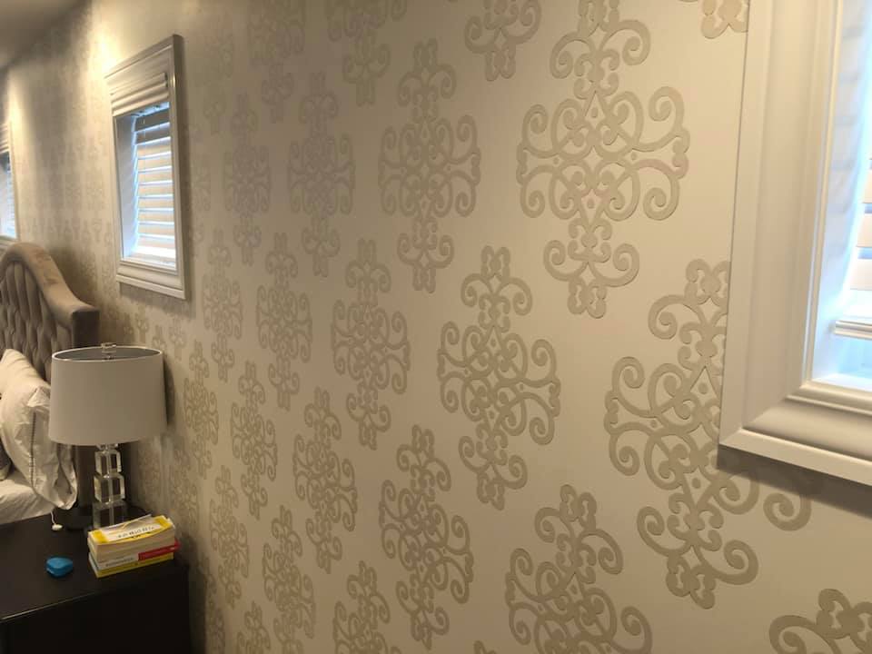 A bedroom with a bed , nightstand , lamp and a wall with a pattern on it.