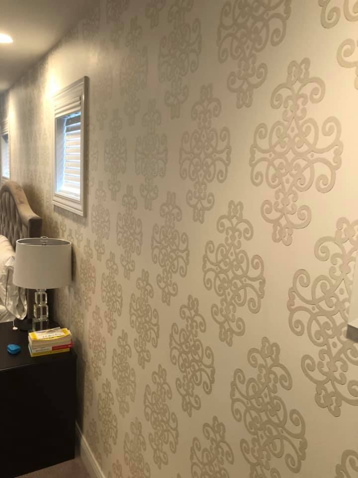 A bedroom with a bed , nightstand , lamp and a wall with a pattern on it.