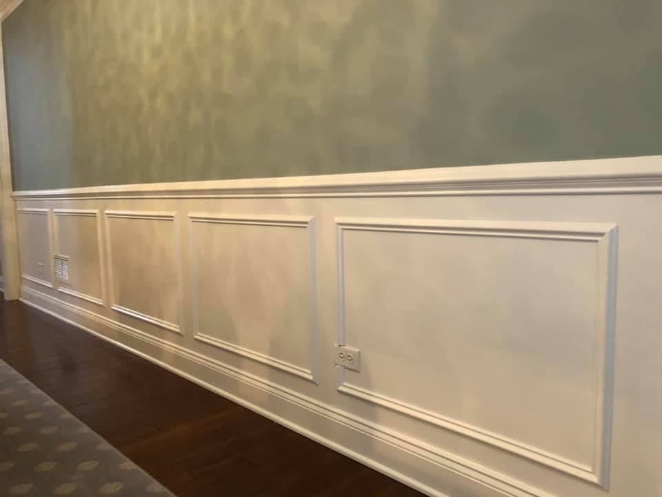 A hallway with a long white wall and a wooden floor.