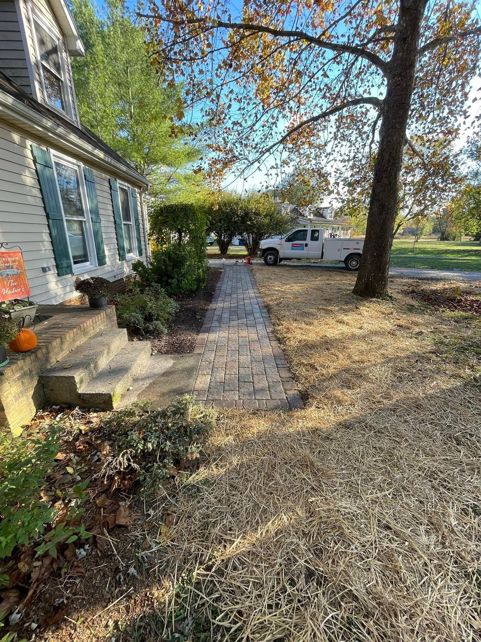 Brick path leads to house with autumn leaves and service van.