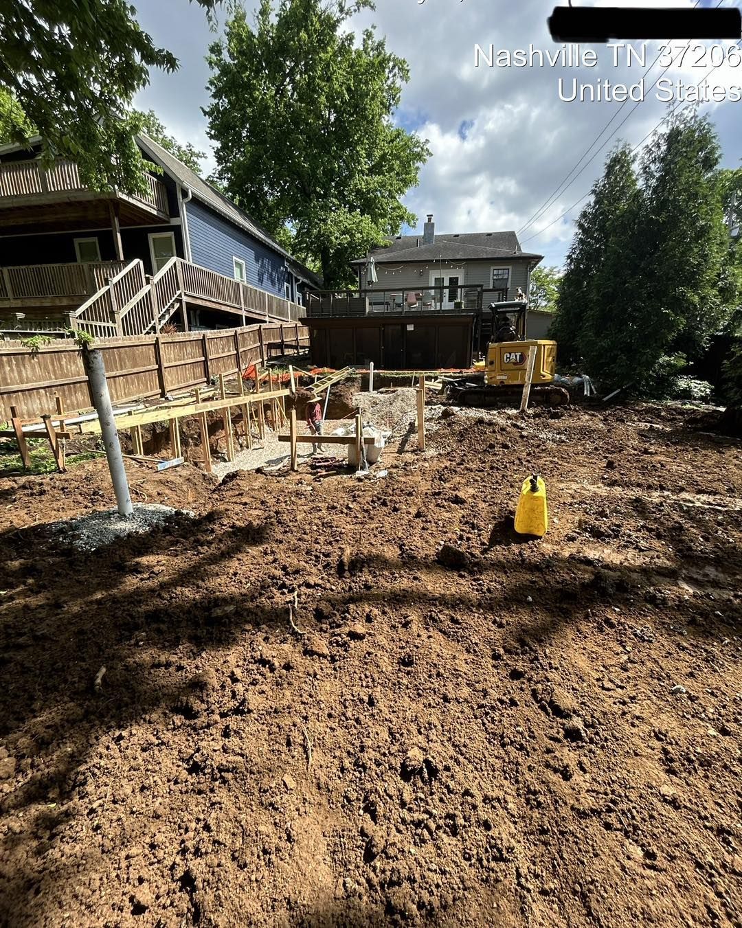 Construction site with exposed foundations, dirt, and heavy machinery. Houses and trees in the background, Nashville.