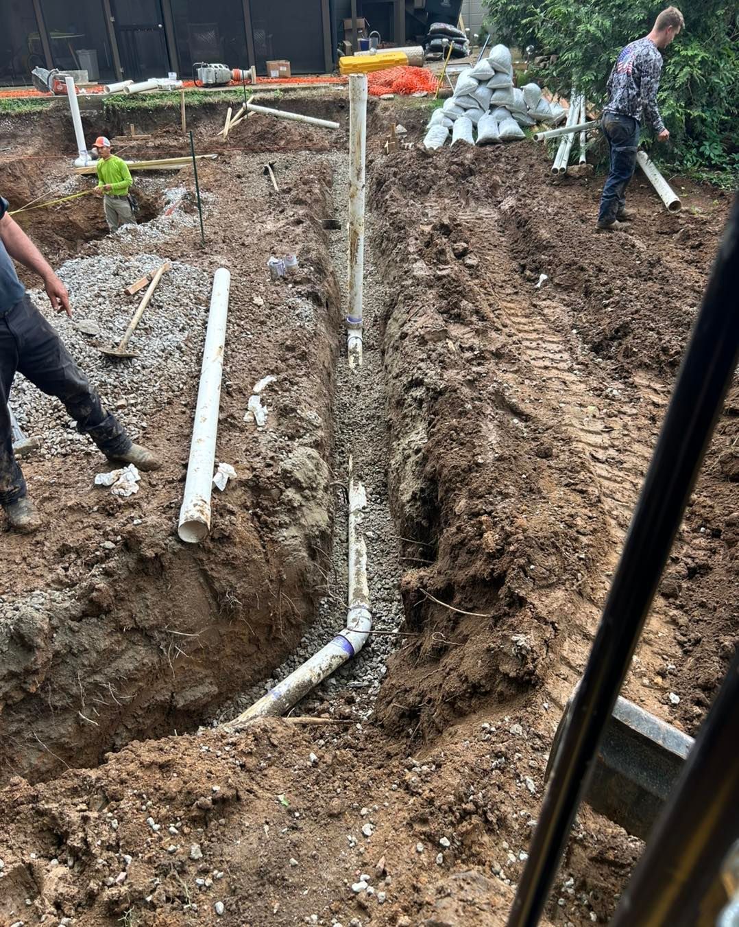 Construction site with trenches, pipes, gravel, and workers installing plumbing.