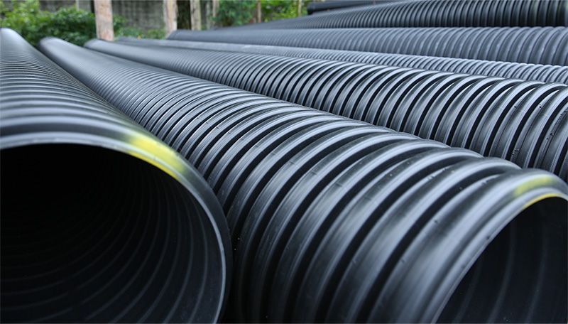 Three yellow excavators on a grassy patch near a small building and trees; some excavation work is underway.