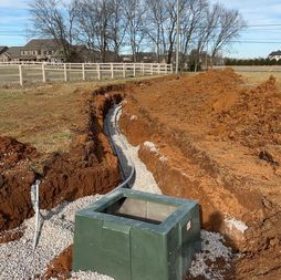 Trench with buried conduit leading to a green utility box in a field. Earthmoving project underway.