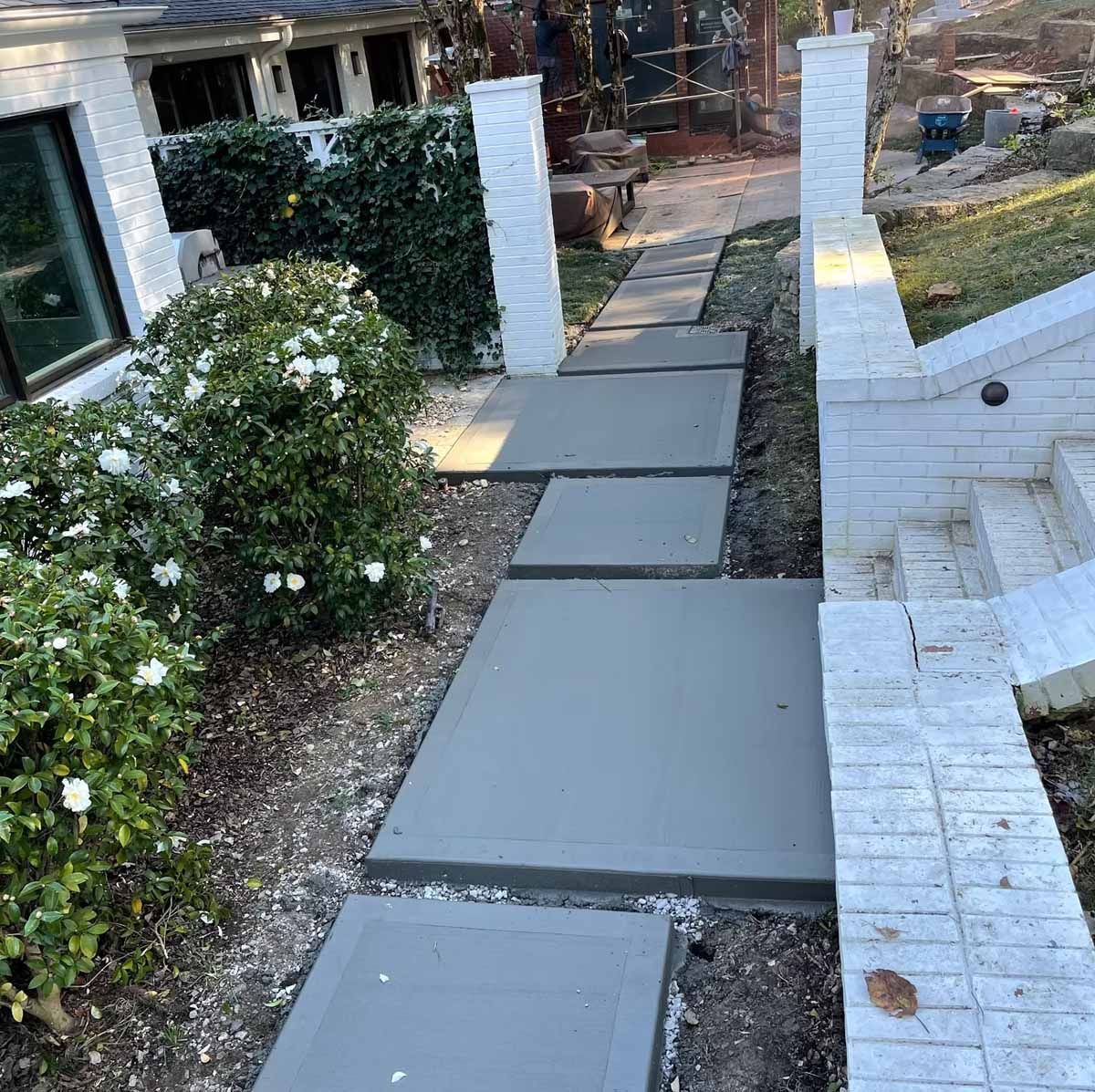 Concrete pathway with square stepping stones between decorative pillars.