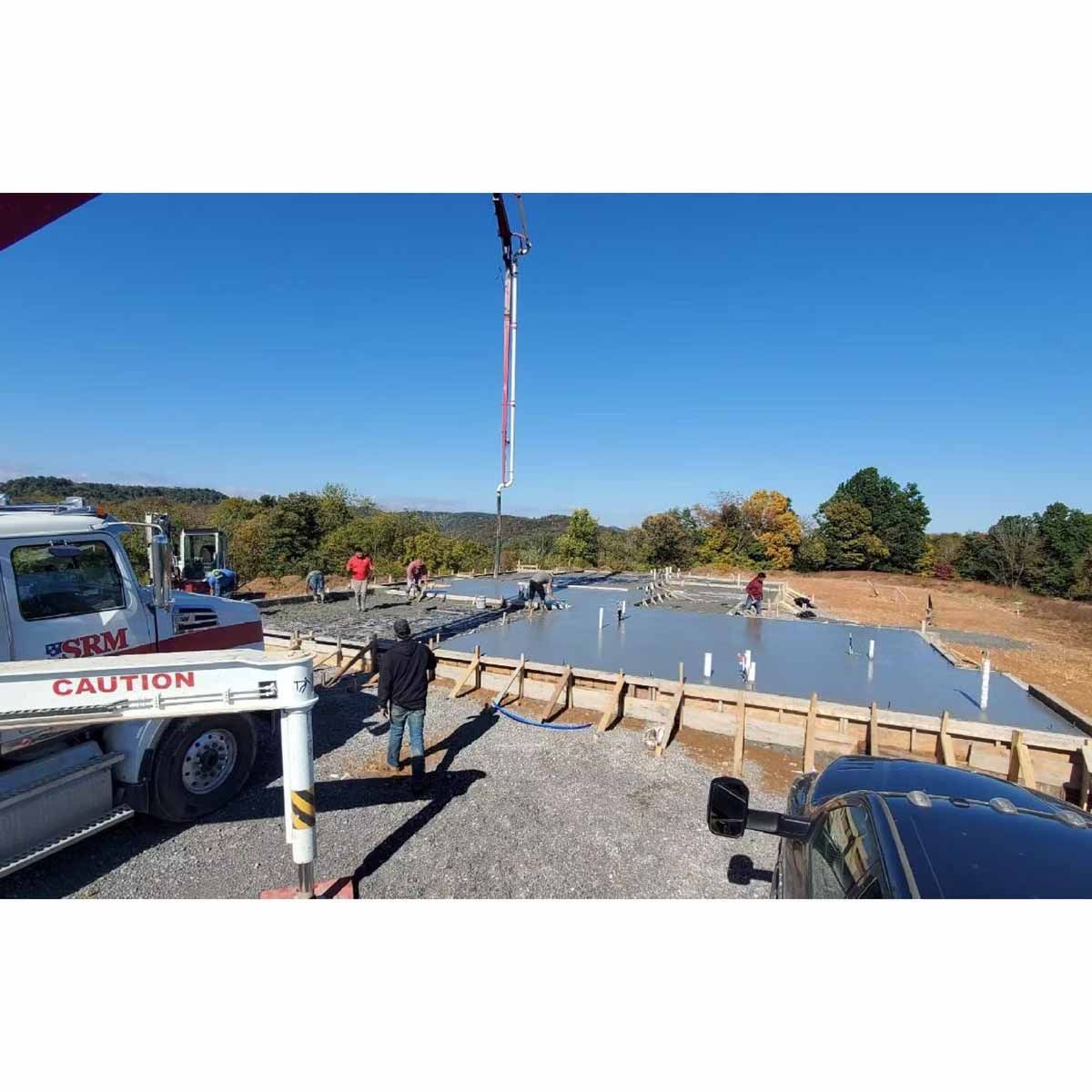 Concrete foundation being poured, construction workers, concrete truck, pump, blue sky, outdoor setting.