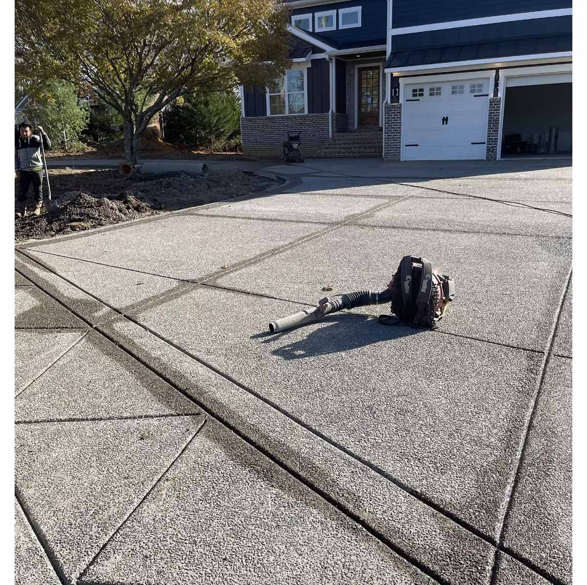 A leaf blower on a gray concrete driveway outside a blue house.