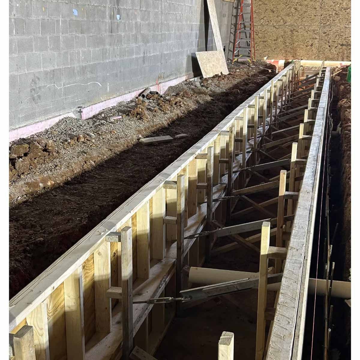 Wooden formwork for a concrete structure in a construction site excavation; soil, gravel, and concrete block walls.