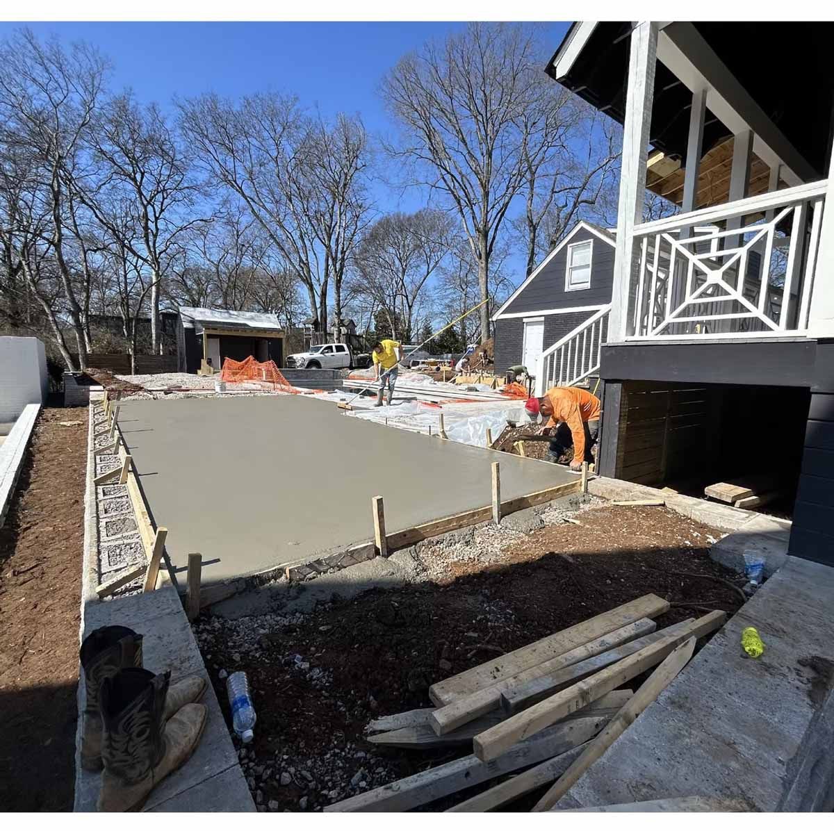 Construction site with workers pouring concrete slab. Brown and grey tones. Clear sky.