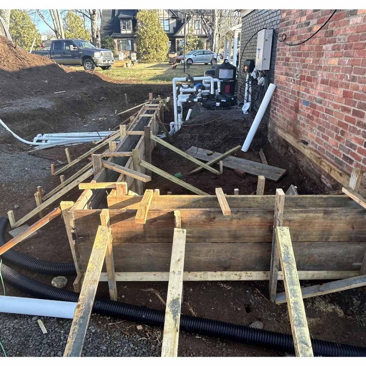 Wooden forms for a foundation wall are being built beside a brick building.