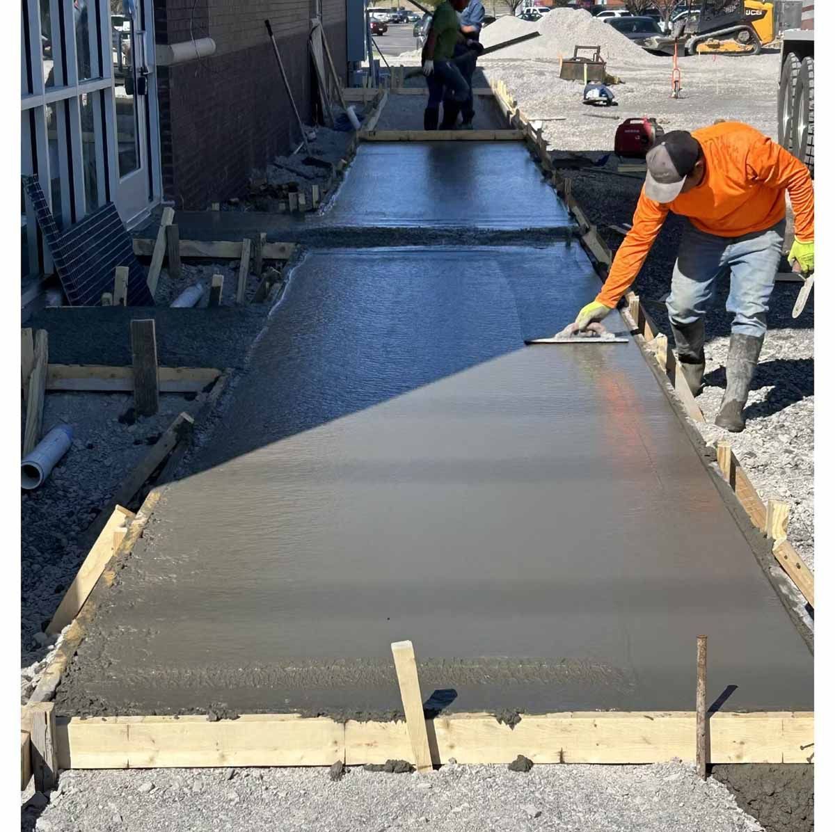 Construction worker smoothing wet concrete sidewalk with a trowel.