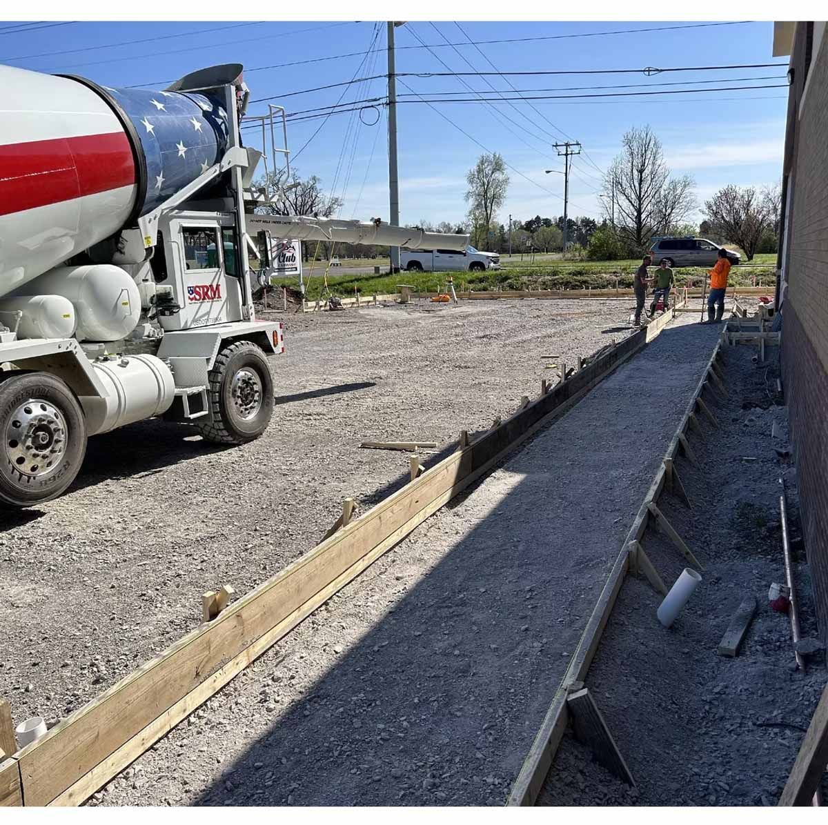 Cement truck pouring concrete for a walkway construction site. Workers leveling the gravel.
