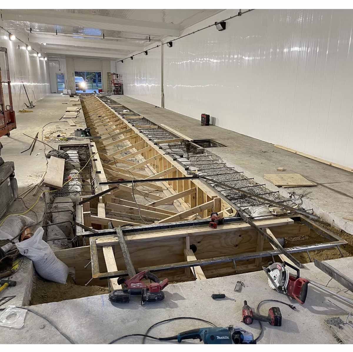 Construction site: Interior view of a long, narrow space with exposed framework and power tools, white walls.