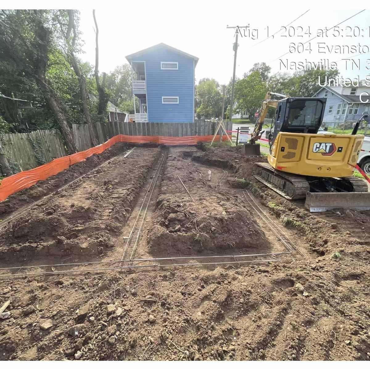 Construction site with small excavator in Nashville, TN. Dirt, orange barrier, and blue house.